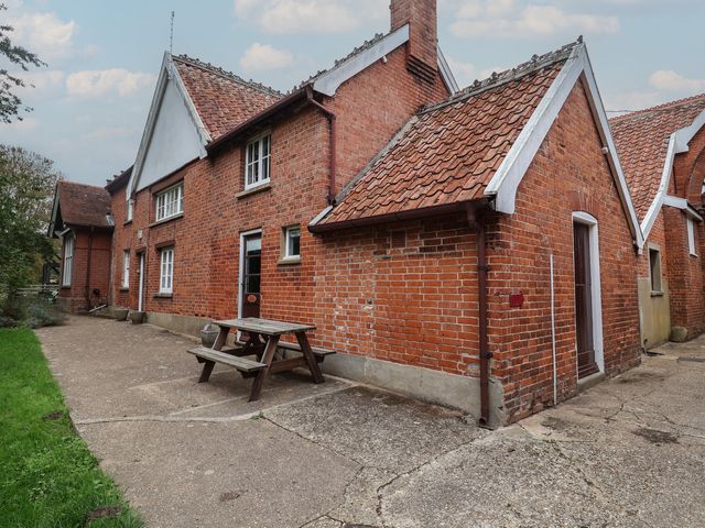 An outdoor view of a brick house with a table and bench at Duchess Cottage Woodbridge
