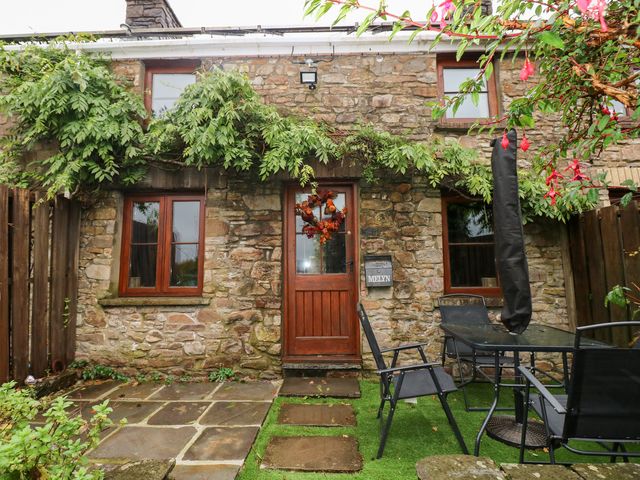 An exterior view of a stone cottage with a garden table and chairs at Melyn in Aberdare