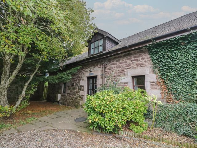A stone building with windows and a doorway surrounded by greenery at The Cottage in Perth