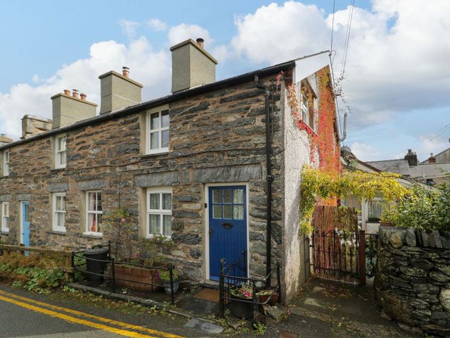 An outdoor view of a stone house with a blue door and flowers at Noddfa Penmachno