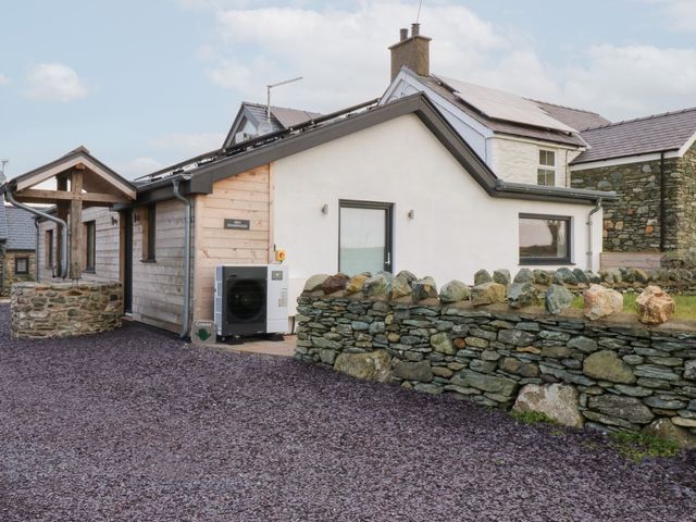 An exterior view of a house with a stone wall and driveway at Hen Penmynydd in Llanfwrog near Llanfachraeth