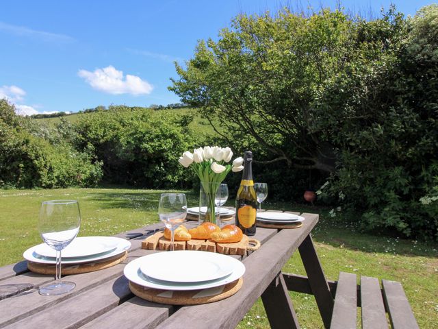 A dining table set with wine glasses, plates, a bottle and flowers at 3 Brook Cottages in Hope Cove