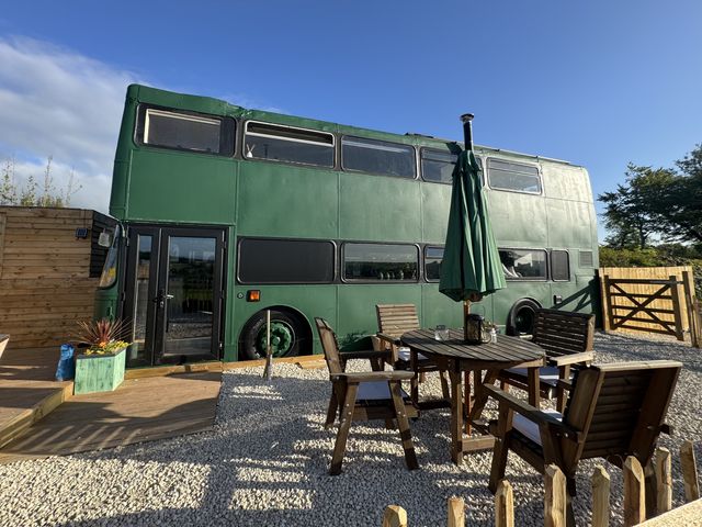 A green double-decker bus with a table and chairs outside at The Bus on the Hill, Huntsham near Bampton, Devon