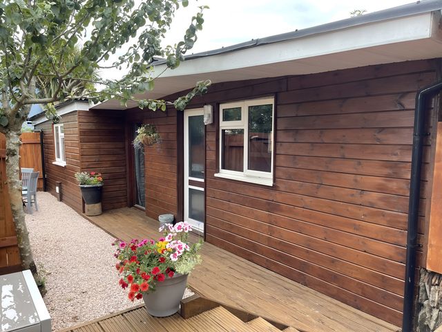 Exterior view of a wooden house with flower pots and seating area at Little Russets