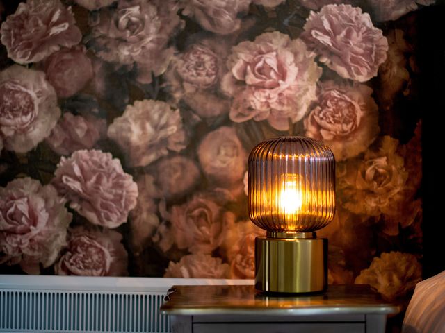 A lamp on a table with a floral wall at Stay Robun