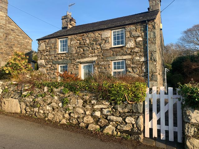 A stone house with a white gate and greenery at Bwthyn Nain