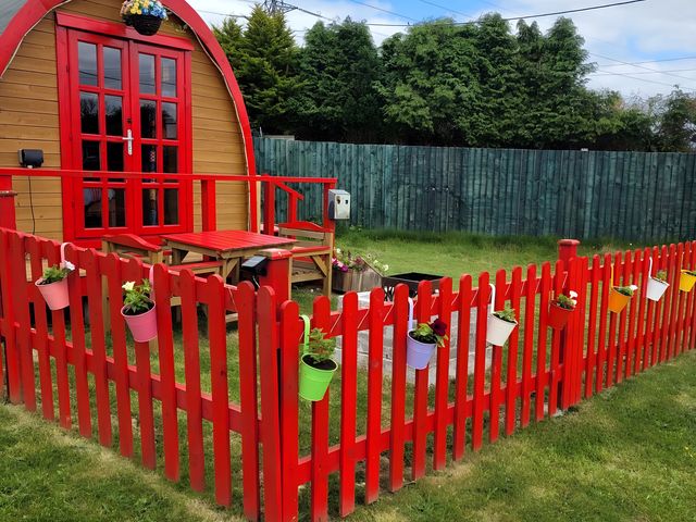 A wooden structure with a red fence and flower pots in the garden at St Austell Glamping