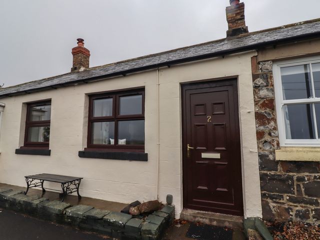 An outdoor view of a cottage with a bench and door at Sunny Brae in Alnwick