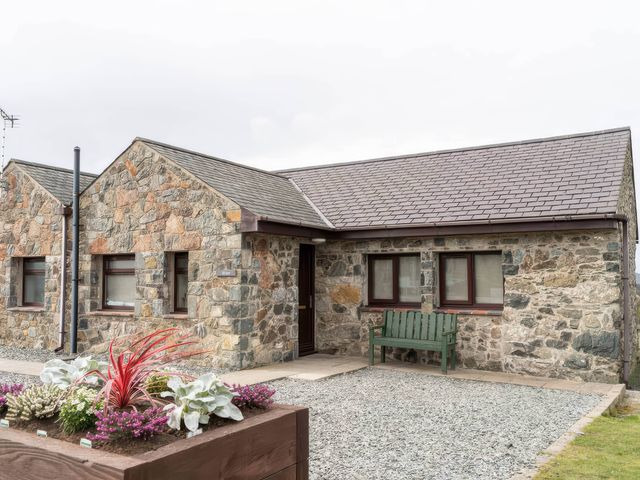 A stone house with a gravel area and bench at Wren Cottage in Llangaffo
