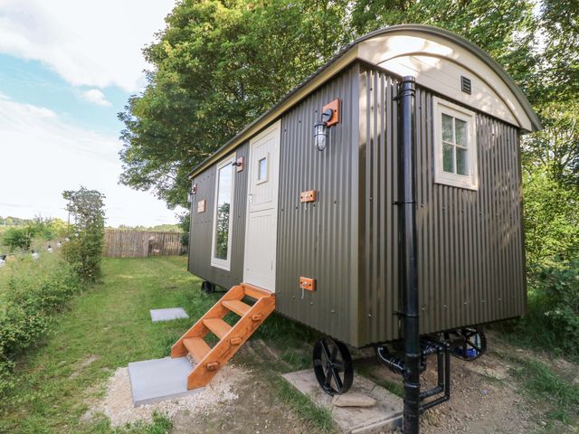 A shepherd's hut with stairs and a doorway in a grassy area at Kingfisher Hut