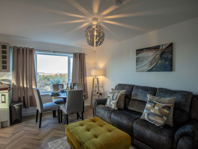 A living room with a sofa, dining area, and curtains at 365 South Boisdale, Daliburgh, Isle Of South Uist