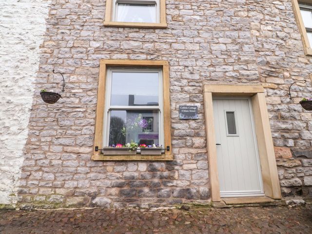 An outdoor view of a stone cottage with a door and flower box at Cobble Cottage in Gisburn