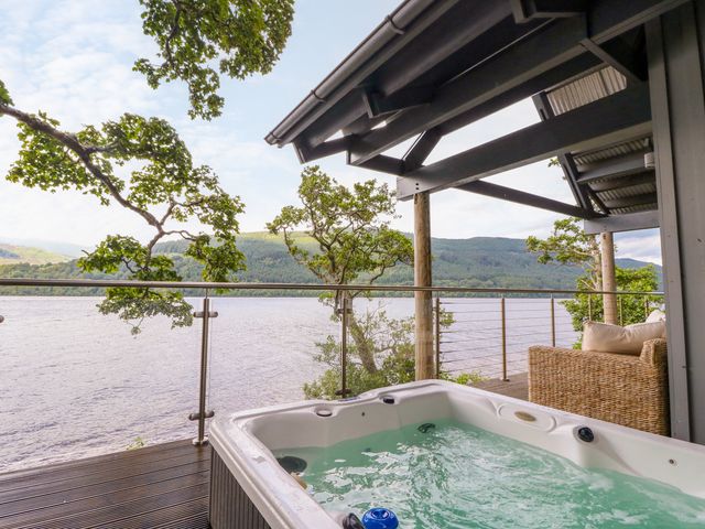 An outdoor area with a hot tub and seating overlooking the lake at Dipper Boathouse in Killin