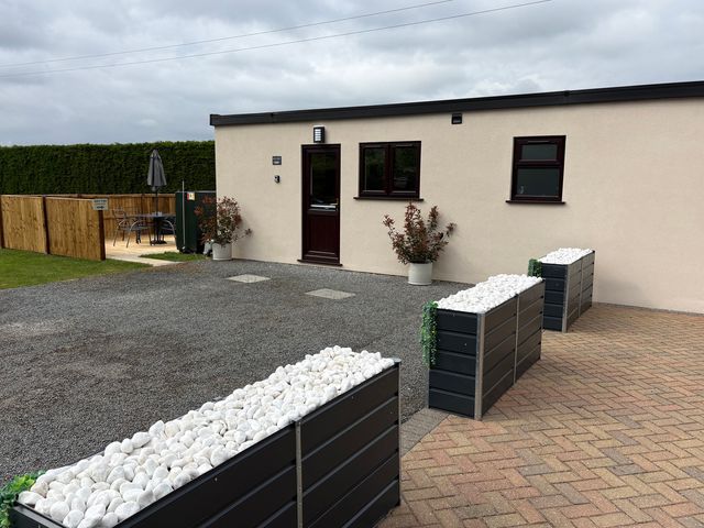 An outdoor area with a house, gravel driveway, table, chairs, and planters at Aloe Lodge in Banham