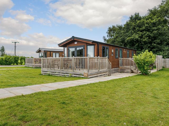 A lodge with a deck and surroundings at Alder Waterside Spa Carlton Miniott near Thirsk