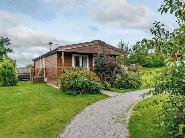 A cabin surrounded by grass and bushes at Fir Tree Waterside Spa Carlton Miniott near Thirsk