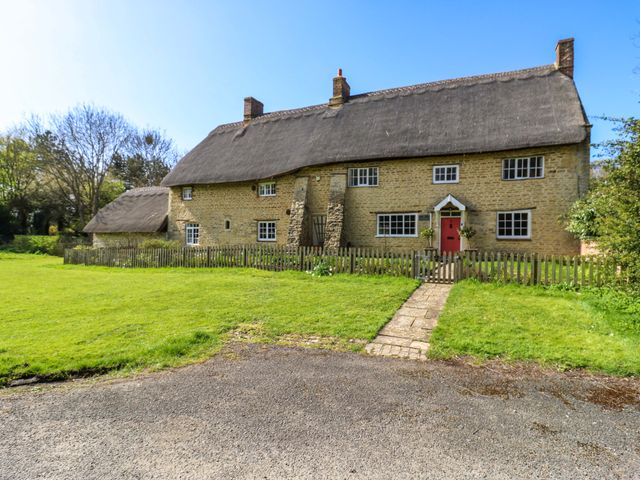 A cottage with a thatched roof and stone walls at Manor Farm Cottages in Loughton, Milton Keynes