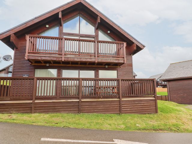 A wooden lodge with a balcony and decked area at 65 Benasa Lodge at Winnard's Perch near St Columb Major