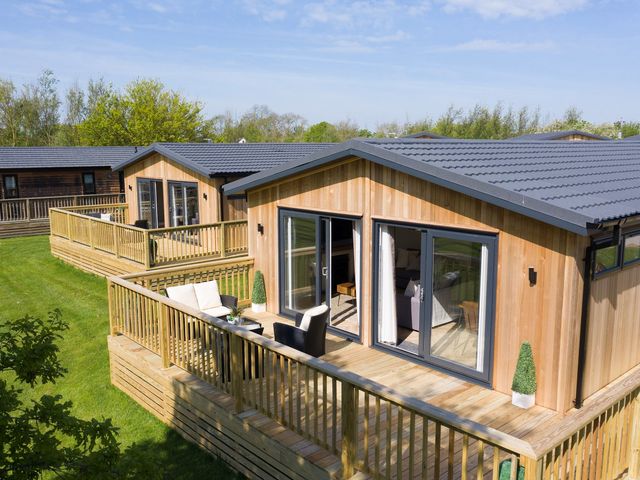 A wooden deck with chairs in front of cabins at Dovecote in Waltham