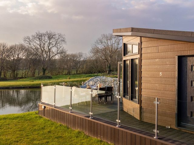 An outdoor deck with a table and chairs beside a lake at Lake View Spa in Praze-An-Beeble