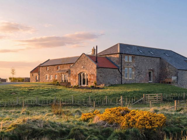 A stone house with grass and trees at The Old Watermill Beadnell