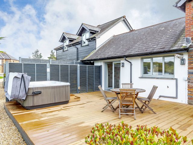 An outdoor area with a hot tub and a wooden table with chairs at 4C2 Summerleaze Garden Cottage 2 Spa Bude