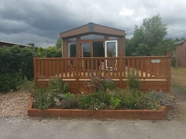 A lodge with a wooden deck and flower planters at Fern Lodge in Stowmarket