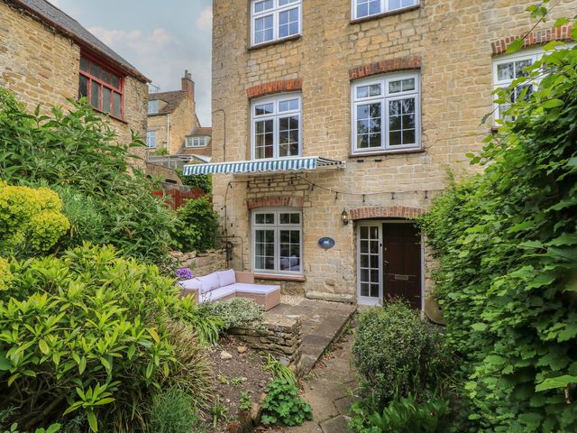 A garden with a house and seating area at Waterloo Mill Cottage in Wotton-Under-Edge
