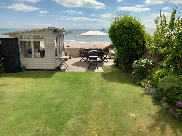 A garden with a shed and seating area overlooking the beach at Beach Haven 116 Leven