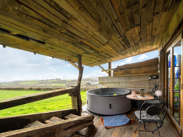 A wooden deck with a hot tub and a table with a chair at The Retreat Cabin in Llanelli
