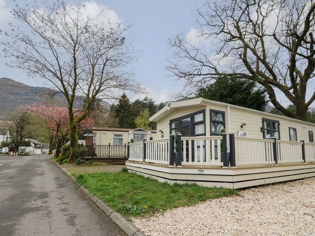 A caravan parked on a gravel area surrounded by trees at No. 59 Loch Lomond Holiday home Crianlarich