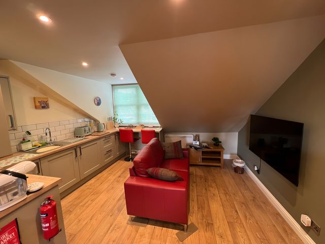 A living room with a red sofa and kitchen area at 1 Bed Studio in Pitlochry