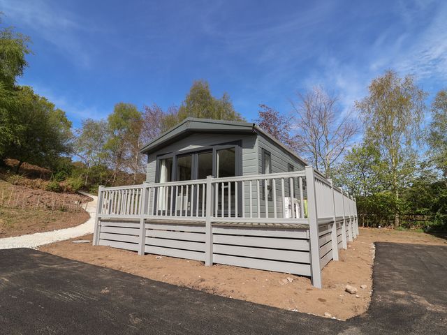 A log cabin with decking and railings surrounded by trees at No.6 - The Pines in Delamere