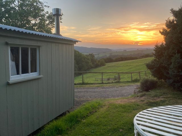 A hut with a chimney next to grass and a sunset view at Cosy Shepherd’s Hut Longhope