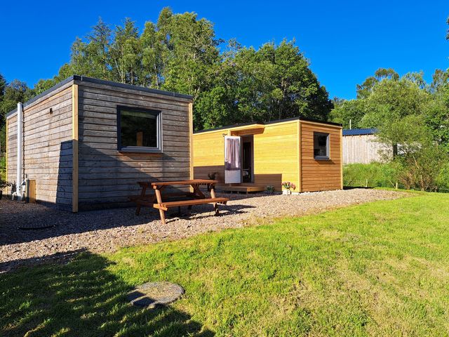 Two wooden cabins and a picnic table in an outdoor area at The Posh Bothy in Roy Bridge