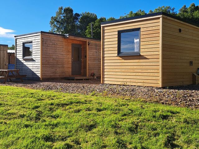 Two wooden cabins with a gravel area and grass at The Posh Bothy 2 Roy Bridge