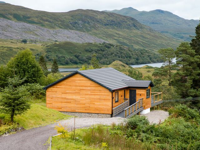 A house with a deck and surrounding landscape at Pinemarten Lodge Crianlarich
