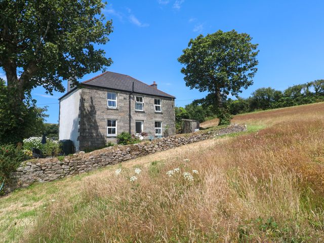A house with a stone wall and trees in a field at Halwyn Farm in Helston