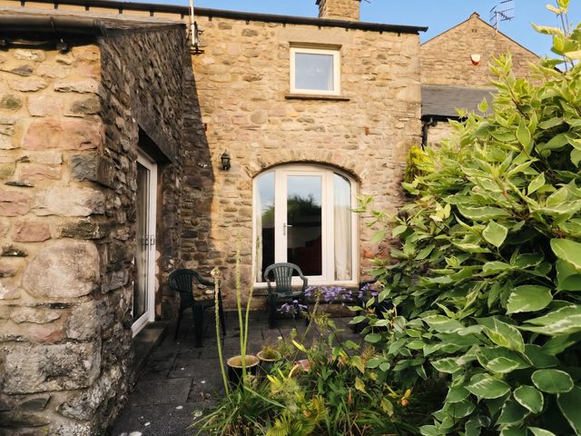 An outdoor area with stone wall, door, window, and chairs at The Spinney near Milnthorpe