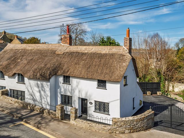 A cottage with a thatched roof and stone wall at Bridge Cottage in Chideock