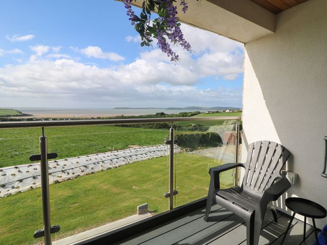 A balcony with a chair and table overlooking a field and sea at Ard Uisce @ Estuary Bliss Duncannon, County Wexford