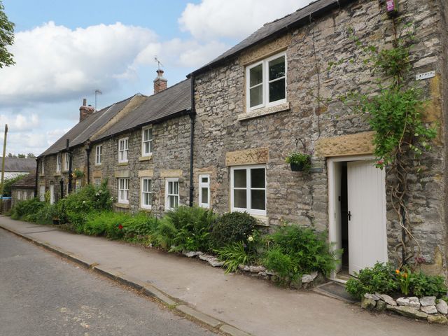 A stone building with windows and plants at Hope Cottage in Great Longstone