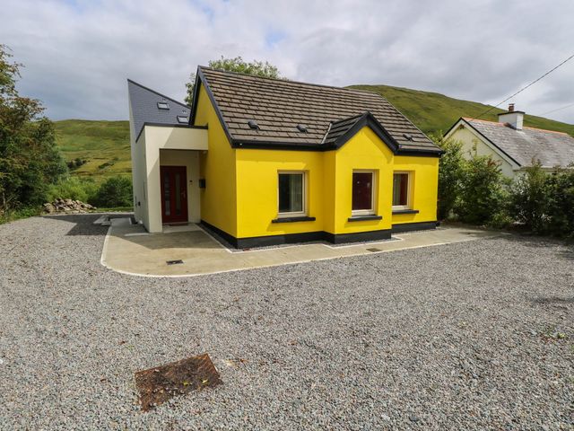 A house with a yellow exterior and a gravel driveway at The Cottage in Leenane, County Galway