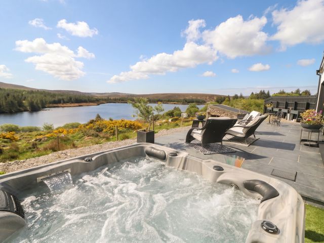 An outdoor area with a hot tub and chairs overlooking a lake at Hanowen House in Dungloe, County Donegal