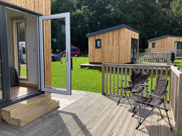 An outdoor area with a deck, chairs, and wooden lodges at Sherwood Pines - Cosy Pod 2 near Edwinstowe