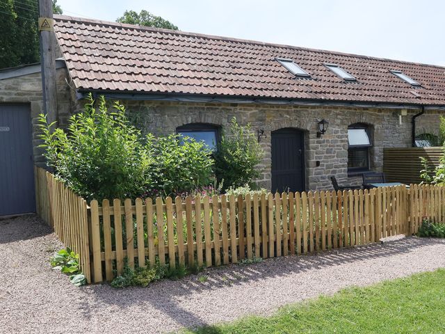 An outdoor view of a stone cottage with a wooden fence at Castle Rag in Parkend