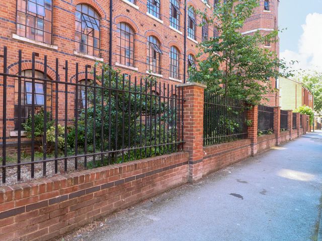 An exterior view of a brick building with a fence and plants near a pathway at Apartments 212 in Nottingham