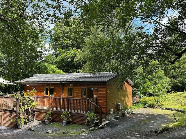 A wooden cabin with a deck surrounded by greenery at Owls House - White Cross Bay Windermere