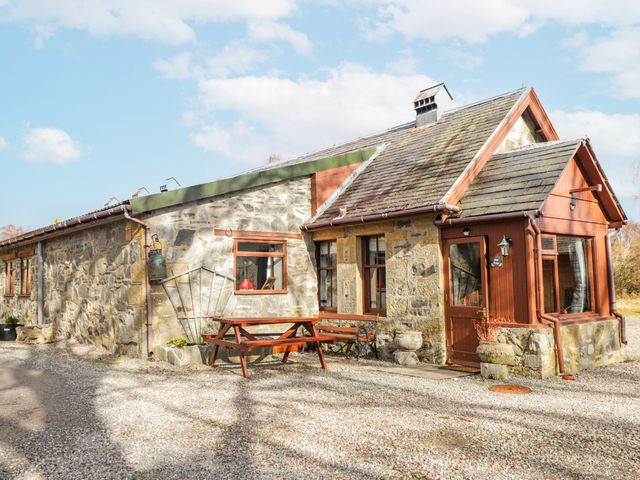 A stone cottage with a table and benches outside at Islay Cottage in Kincraig