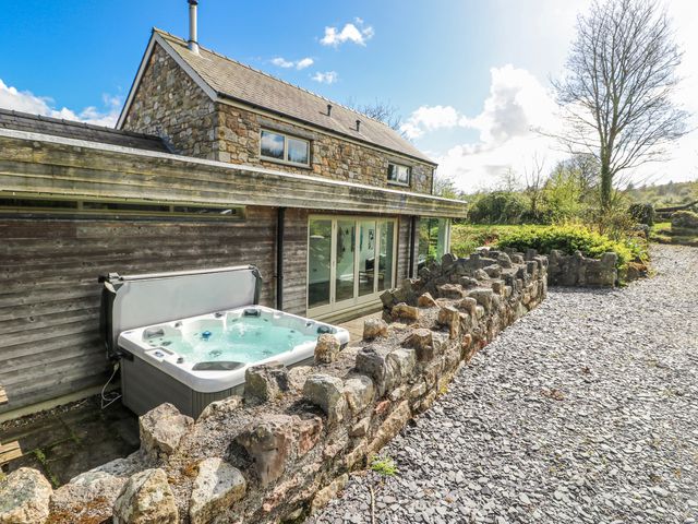 An outdoor area featuring a hot tub and stone wall at Too Hoots in Lligwy